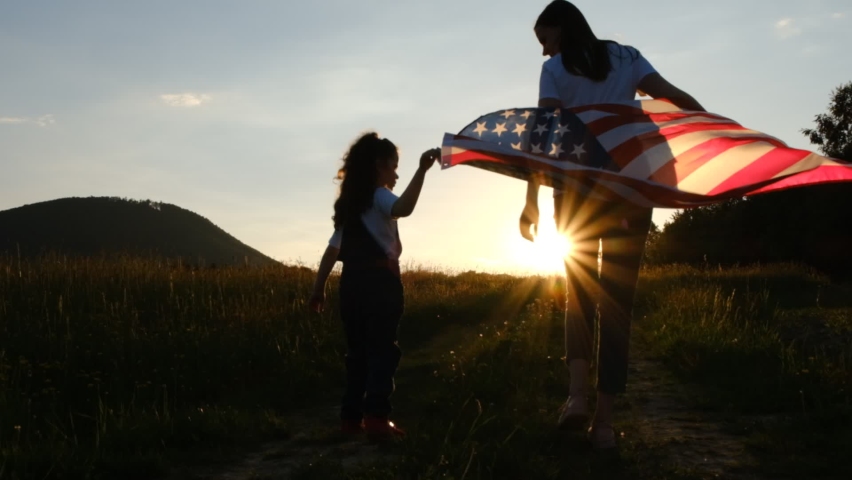 Selective focus of mother with daughter run meadow in wind with united states flag on background mountains during epic sunset. Concept of Memorial Day or 4th of July, Independence Day, Veterans Day | Shutterstock HD Video #1073848811