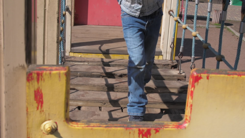 Careful blonde junior schoolgirl walks along suspension bridge boards at castle playground
