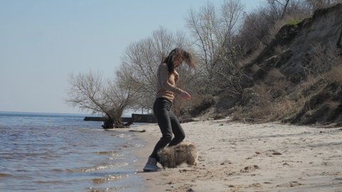 Smiling young woman with long loose hair jumps and plays with furry Shih tzu dog on sandy beach against bare tree slow motion. Concept healthy training