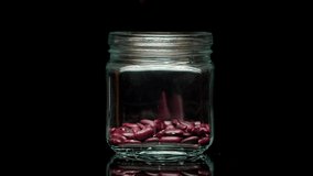 Close-up of falling down red beans into glass jar on black background. Shooting of haricots in studio. Macro footage of pouring out the beans. Food cooking video. 