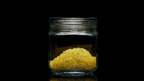 Close-up of falling down bulgur into glass jar on black background. Shooting of seeds and groats in studio. Macro footage of pouring out the grits. Food cooking video. 
