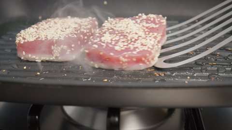 Flipping a steak of yellowfin tuna on a grilling pan in 4K. Concept turning on the other side and frying and cooking tuna steak in slow motion.