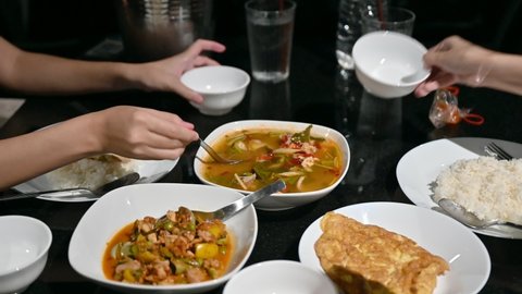 Group of friends eating variety thai food with spicy soup, omelet, fried fish, fried tofu on dining table