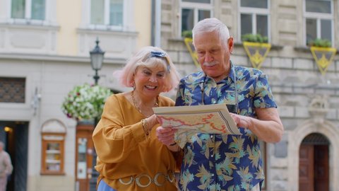 Senior couple grandmother and grandfather tourists in stylish clothing looking for a place to go in new city Lviv, Ukraine, using paper map. Elderly family man, woman on holidays vacation traveling