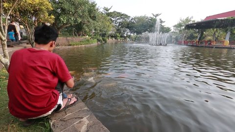 A father and his son are feeding fish in the Purwokerto City Park Balai Kemambang . Central Java, Indonesia.June 8, 2021