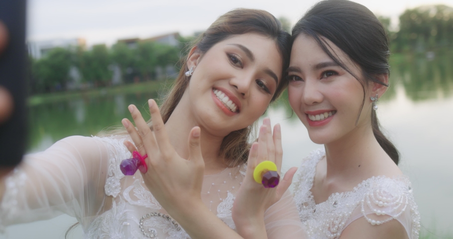 Happy Asian Lesbian Married Couple On Wedding Day. The Married Couple Happily Chatting Over Video Calls With Friends.