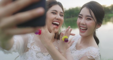 Happy Asian Lesbian Married Couple On Wedding Day. The Married Couple Happily Chatting Over Video Calls With Friends.
