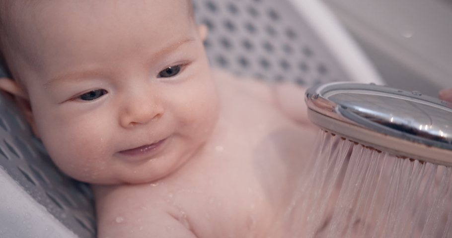 Hygienic procedures for newborn. Bathing the baby in the bathroom. Happy baby in the shower. The child is poured with warm water from the shower. | Shutterstock HD Video #1073879972