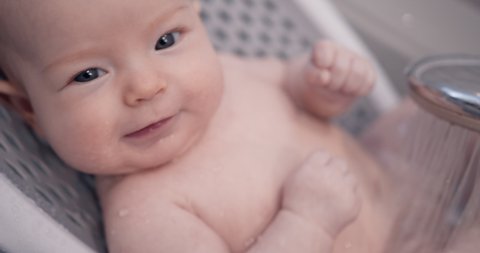 Hygienic procedures for newborn. Bathing the baby in the bathroom. Happy baby in the shower. The child is poured with warm water from the shower.
