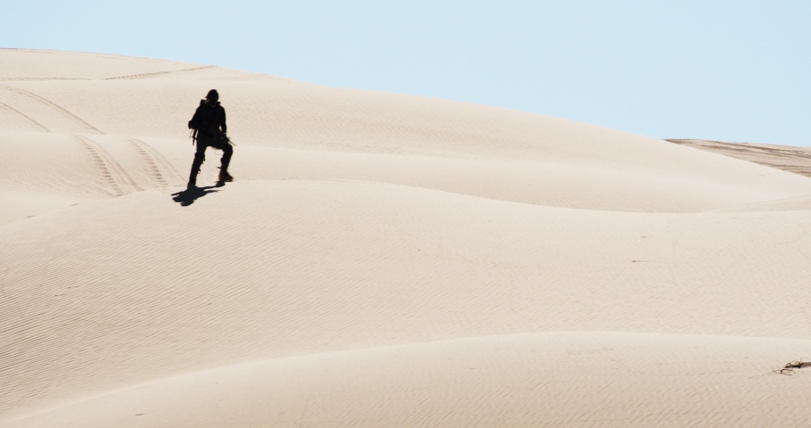 Silhouetted soldier wandering and running alone over sand dunes in desert, America