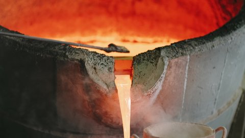 Hot Liquid Metal Stream is Pouring from Induction Foundry Furnace. Yellow Molten Steel. Industrial Oven. Steel casting. Hot metal. Heat. Danger. Heavy industry. Close up, slow motion.
