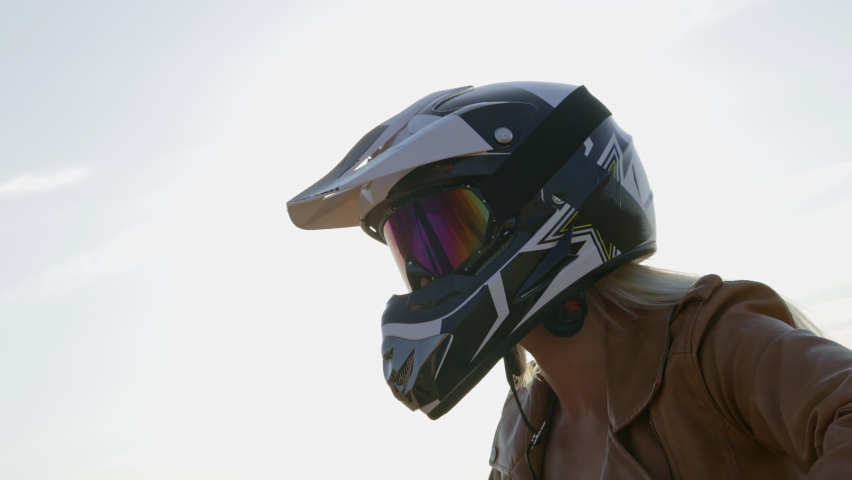 Woman in helmet and leather jacket presses on motorbike brakes handlebar and rides on sand beach by sea on spring day closeup