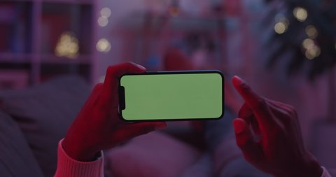 Lviv, Ukraine - February 05, 2021: Close up of male hands holding cell phone in horizontal position and doing swiping with finger. Green mock up screen on mobile. Copy space.