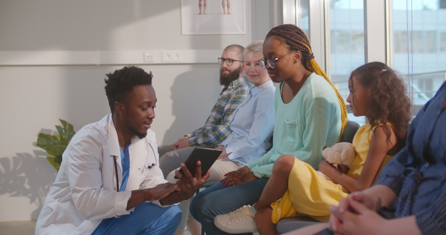 Afro-american male doctor talking to mother and kid in hospital waiting room. Young african woman with daughter sitting in clinic reception area consulting specialist | Shutterstock HD Video #1073887541