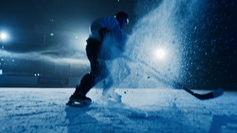 Ice Hockey Rink Arena: Professional Player Training Alone. Skates, Practices Hockey Stop. Determined Athlete with Desire to Win, Be Champion. Dramatic Medium Shot, Cinematic Blue Lighting