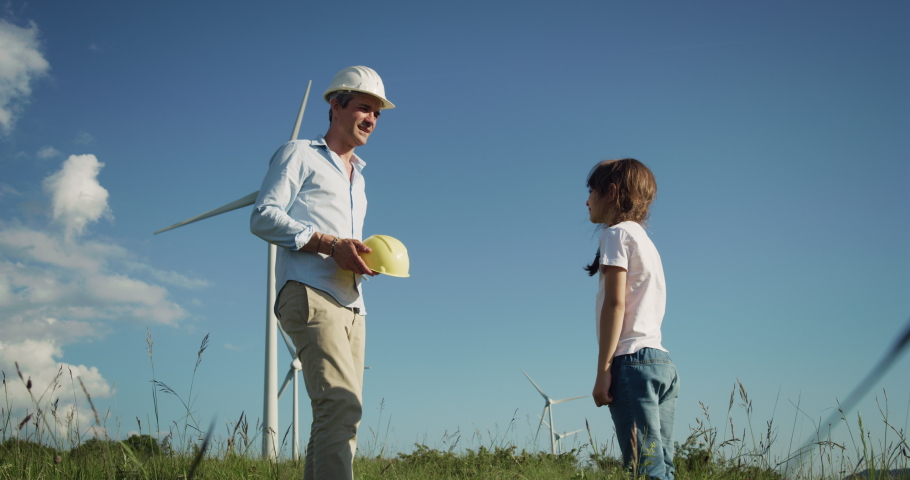 Wind Farm in a Green Field: Proud Dad Putting a Protective Helmet on his Daughter's Head, Hugging Her, Giving Children the Clean Future They Deserve. Father Ensuring Kid's Dream for Sustainable Future Royalty-Free Stock Footage #1073890385