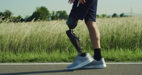 Cinematic close up of man with disability with artificial bionic high technology legs prosthesis running on countryside road.Concept of persons with disabilities active lifestyle,  cyborg