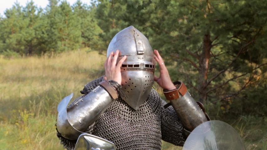 A medieval warrior in full armor, takes off his helmet. A medieval knight on a modern bike.