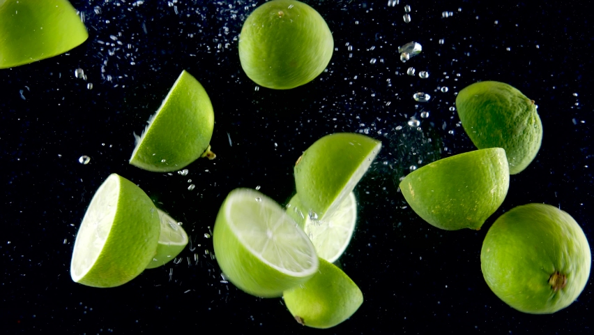 Lime splashing into the water in slow motion. Lots of limes falling slowly on a black background. Organic green citrus isolated on black background. Fresh water with fruits. Royalty-Free Stock Footage #1073892206