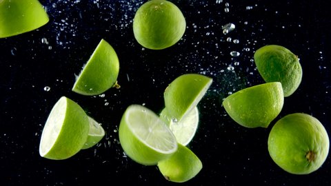 Lime splashing into the water in slow motion. Lots of limes falling slowly on a black background. Organic green citrus isolated on black background. Fresh water with fruits.