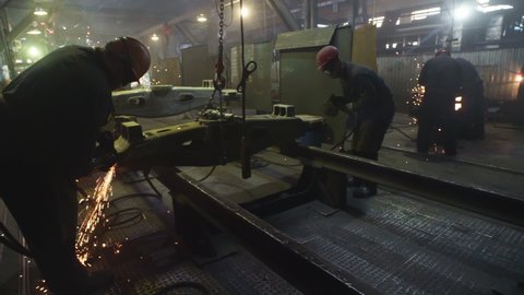 Group of Male Workers Processing Large Metal Structure From Opposite Sides With Circular Sawing Tools. Sparks Scattering. Inside A Manufacturing Facility. Production Of Rail Cars. Dangerous Profession