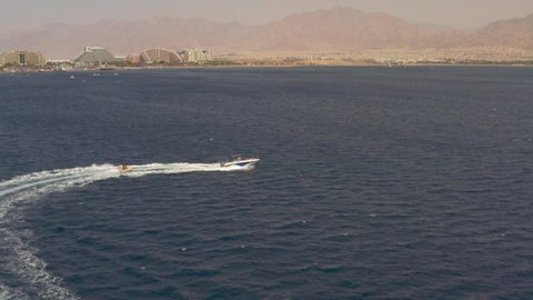 Fast Speedboad Dragging Banana boat full of people having fun 
Drone view from Red sea, Eilat Israel


