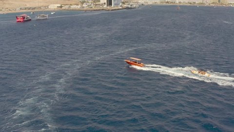 Fast Speedboad Dragging Banana boat full of people having fun 
Drone view from Red sea, Eilat Israel

