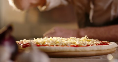 Senior Italian chef putting shredded mozzarella cheese on pizza dough with tomato sauce, cooking pizza with traditional recipe close up 4k footage