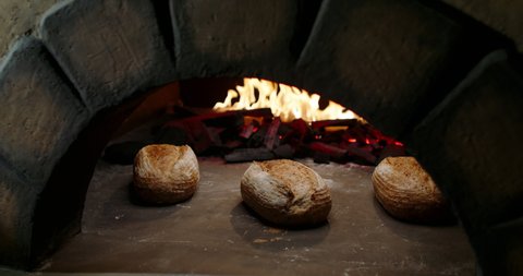 Fresh loaves of organic bread being cooked in authentic stone oven. Traditional bakery worker taking a bread bun out of stove with peel 4k footage
