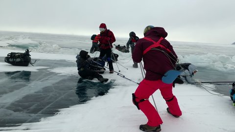 Hurricane wind knocks down tourists traveling on the ice of frozen Lake Baikal in winter. People are blown away and they fall hard and it hurts to turn over on the ice with sledges and backpacks with 