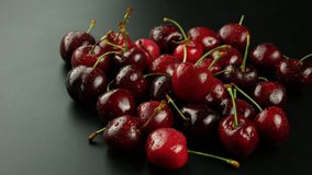 Group of cherry fruits on dark background. Hand takes a cherry from the group and puts it back. 4k video.