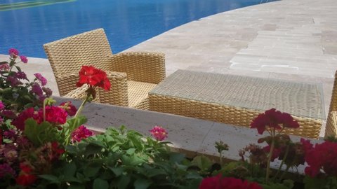 Time lapse summer terrace with wicker rattan chairs and table near pool resort. Red geranium flowers in flowerbed of seaview cafe. Luxury tropical vacation background with nobody