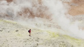 Aerial panning shot on man excursionist walking trough volcano sulfuric smokes, tilt down camera toward crater. Scenic view of Volcano Island travel destination in Sicily, Aeolian Islands