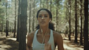 Mixed race female running in forest exercising in nature listening to music with earphones 