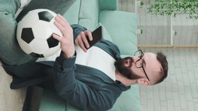 Portrait of an young bearded man standing with soccer ball in hands and talking on the phone on bright room background. Soccer fan, player.