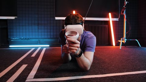 People in virtual reality simulation technology studio. Man shooting in VR game. Oculus glasses gadget, augmented headset gun gaming. Caucasian person in simulator set goggles. Room in neon lightning.