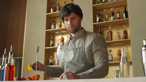 Bartender prepares a cocktail hand stirring a orange summer cocktail with a spoon on the bar counter.