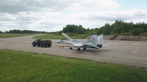 A military tractor pulls a fighter plane towards the runway. Quadrotor filming