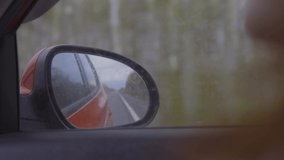 Video shooting in motion, view in the rear view side mirror of a auto, driving a red car along the road