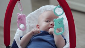 2 month old baby boy in rocking chair playing with hanging toys, infant sensory development. High quality 4k footage