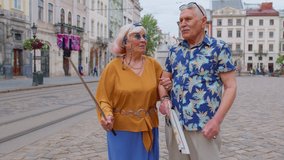 Senior stylish blogger tourists man and woman taking selfie photo portrait, making video call on mobile phone. Elderly travelers grandmother grandfather talking enjoying time together. Summer vacation