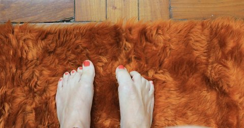 Detail of female feet with pink-painted nails, folding only toes on an orange fur rug