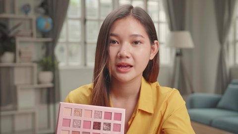 Vlogger Female Showing Eye Shadow Palette. Beauty Blogger Woman Filming Daily Make-Up Routine Tutorial Near Camera On Tripod. Influencer Girl Live Streaming Cosmetics Product Review In Home Studio
