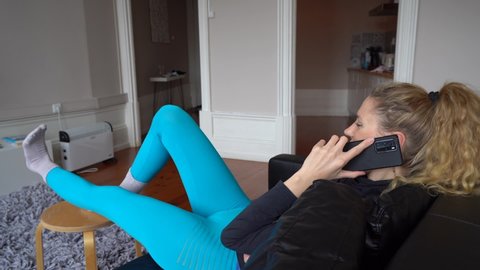 Woman Talking On Phone While Sitting On Couch And Stretching Her Legs - wide shot