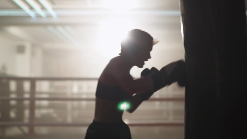 Blurred view, woman fighter trains his punches, beats a punching bag, training day in the boxing gym, strength fit body, the female strikes fast.