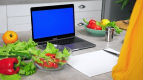Blue screen mock up chroma key monitor display laptop: Woman housewife in home kitchen salt cooked vegetarian delicious salad in glass bowl, study watch online cooking culinary course lesson computer