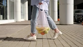 Woman in jeans walking and holding white mesh bag with fruits. Eco friendly, reusable shopping bag. Oranges, apples, bananas in cotton knitted string bag. Zero waste and plastic free concept. - Powered by Shutterstock - Get 15% off with code: PIKWIZARD15