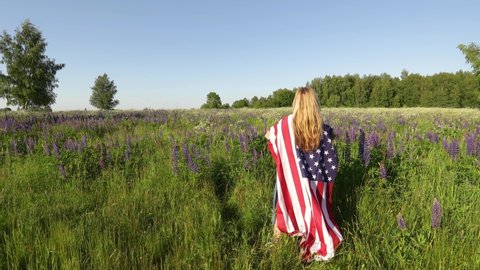 Unrecognizable blond woman wearing american flag stands in the meadow and mourns her fallen soldier husband. Memorial day concept.