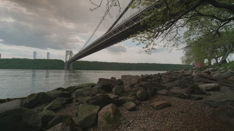 A slow pan from left to right of Hudson River, ending on George Washington Bridge, New York City side. In the distance, skylines of Manhattan and New Jersey, and the treelined beauty of the Palisades.