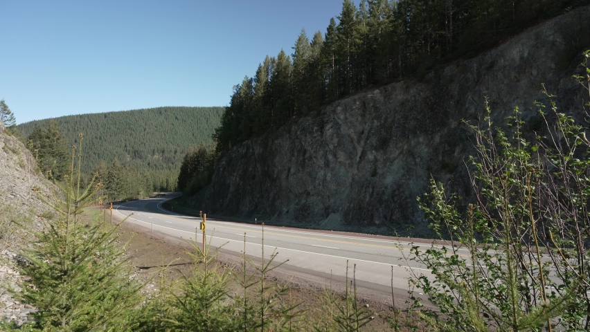 Vehicles travel through a deep rock cut on a mountain highway under blue skies on a spring morning at Silent Rock near Government Camp, OR on Highway 26. Extreme wide angle view, slightly elevated.